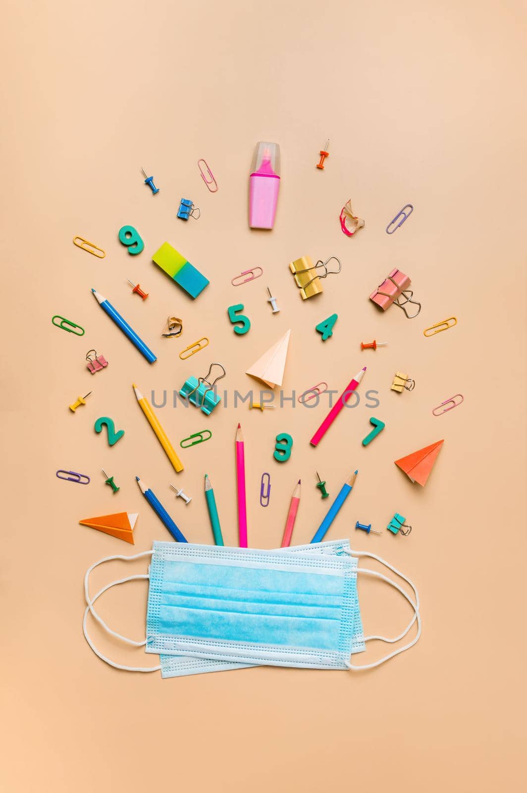 Protective medical mask on creative student desk with colorful modern school supplies on neutral pastel beige background. Top view. Flat lay. Back to school covid19 concept. Vertical