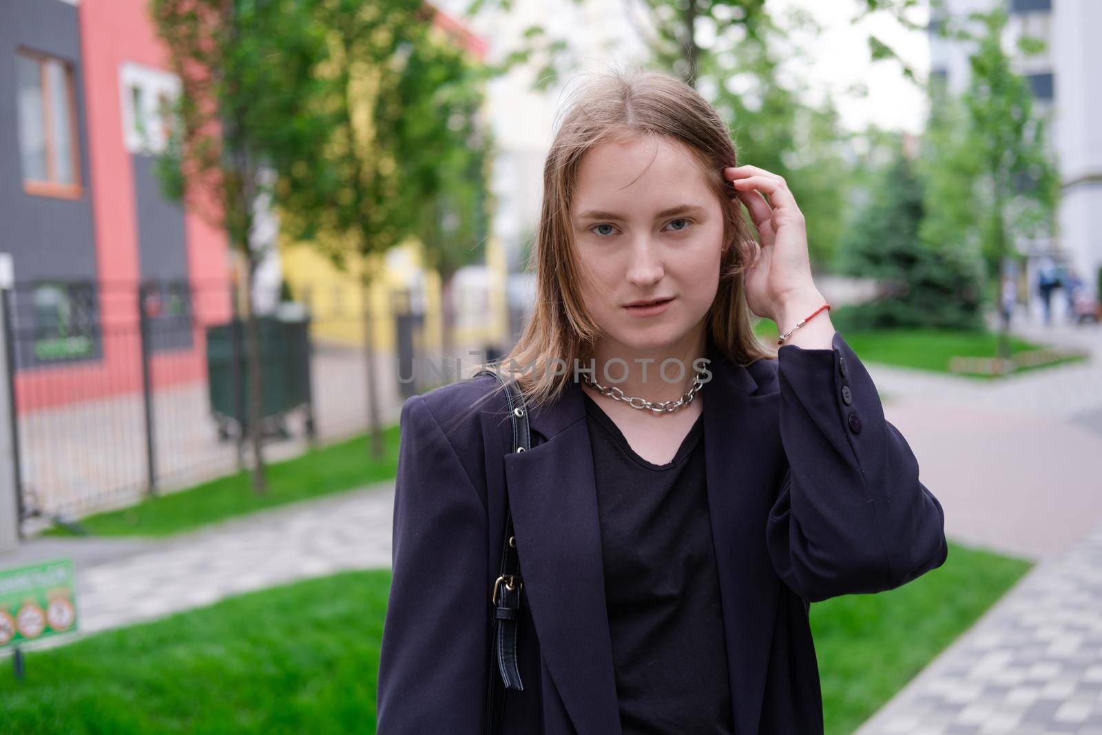 portrait of confident attractive brunette woman in black on background of colorful bright buildings. business woman. feminine. millennial people.