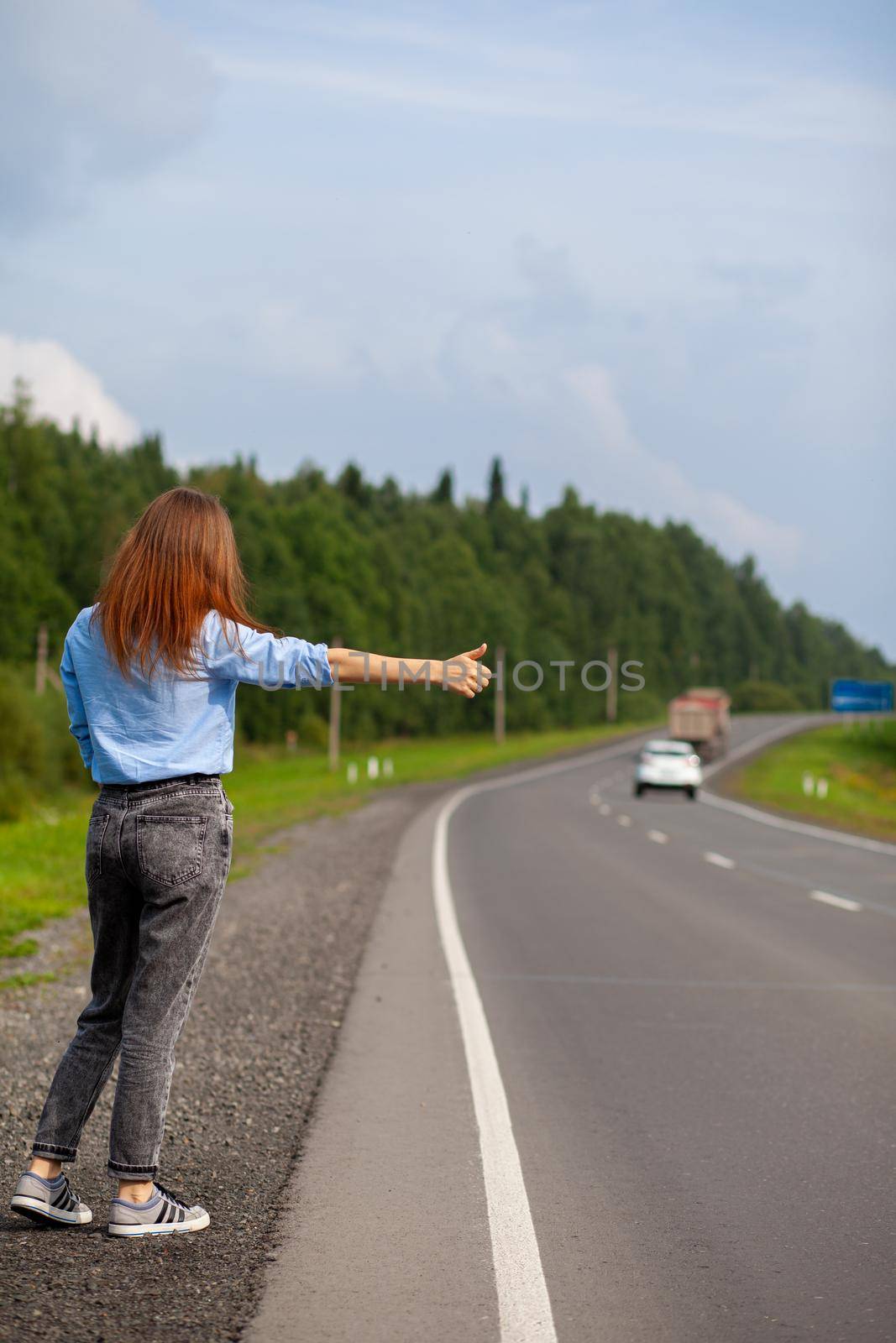 The girl stops the car on the highway with her hand. Stylish woman on the road stops the car go on a journey. A road in the middle of the forest.