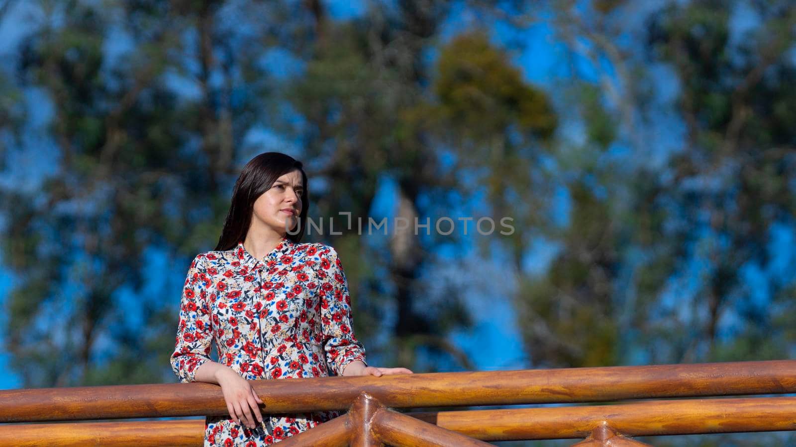 Portrait of beautiful young Latin woman looking to the right with floral design dress standing in the middle of a garden with a background of trees during the morning