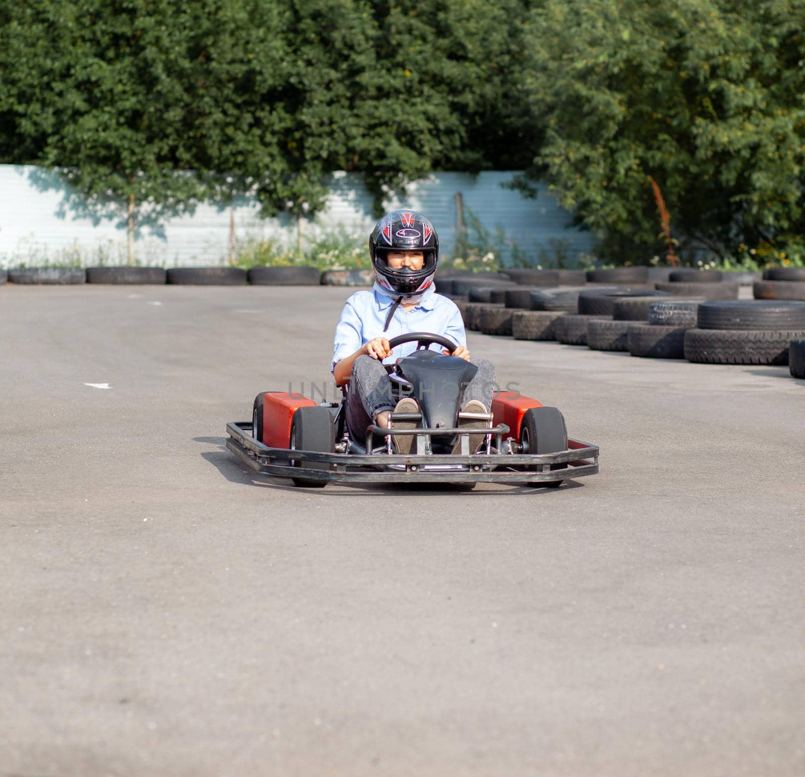 A girl or a woman in a hard hat rides a go-kart on a special track fenced with rubber wheels. Active recreation and sports on transport. Preparation and training for competitions. 