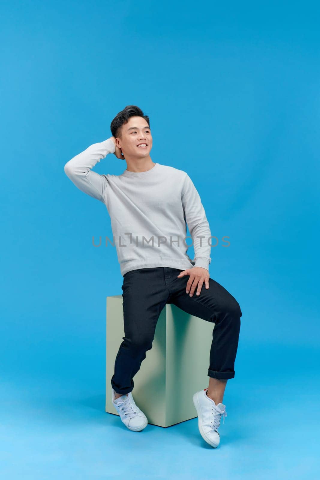 Casual young man sitting on a mint column isolated on blue background