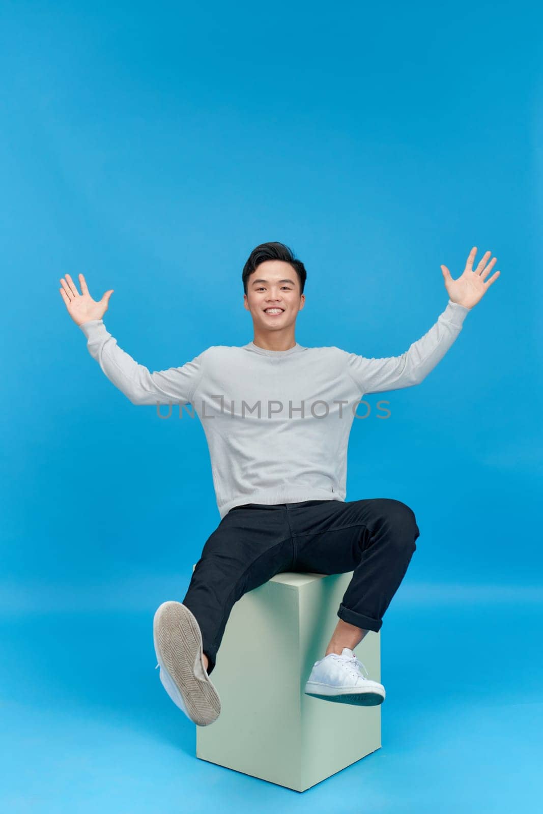 happy handsome young man smiling at camera while sitting isolated on blue by makidotvn