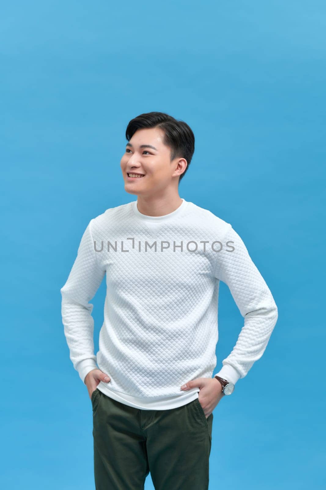 charming cheerful positive young man hold hands pockets isolated on blue background by makidotvn