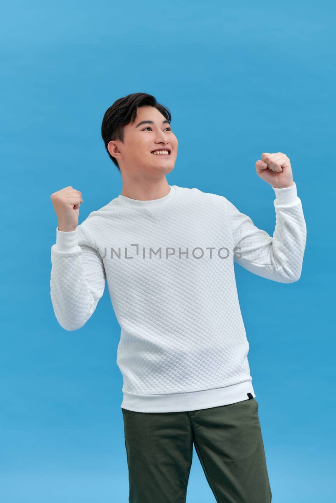 Cheerful excited man standing isolated over blue background, celebrating success by makidotvn