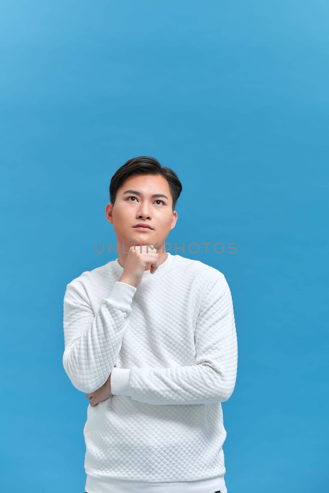 man thinking with hand touching chin in isolated studio blue background by makidotvn