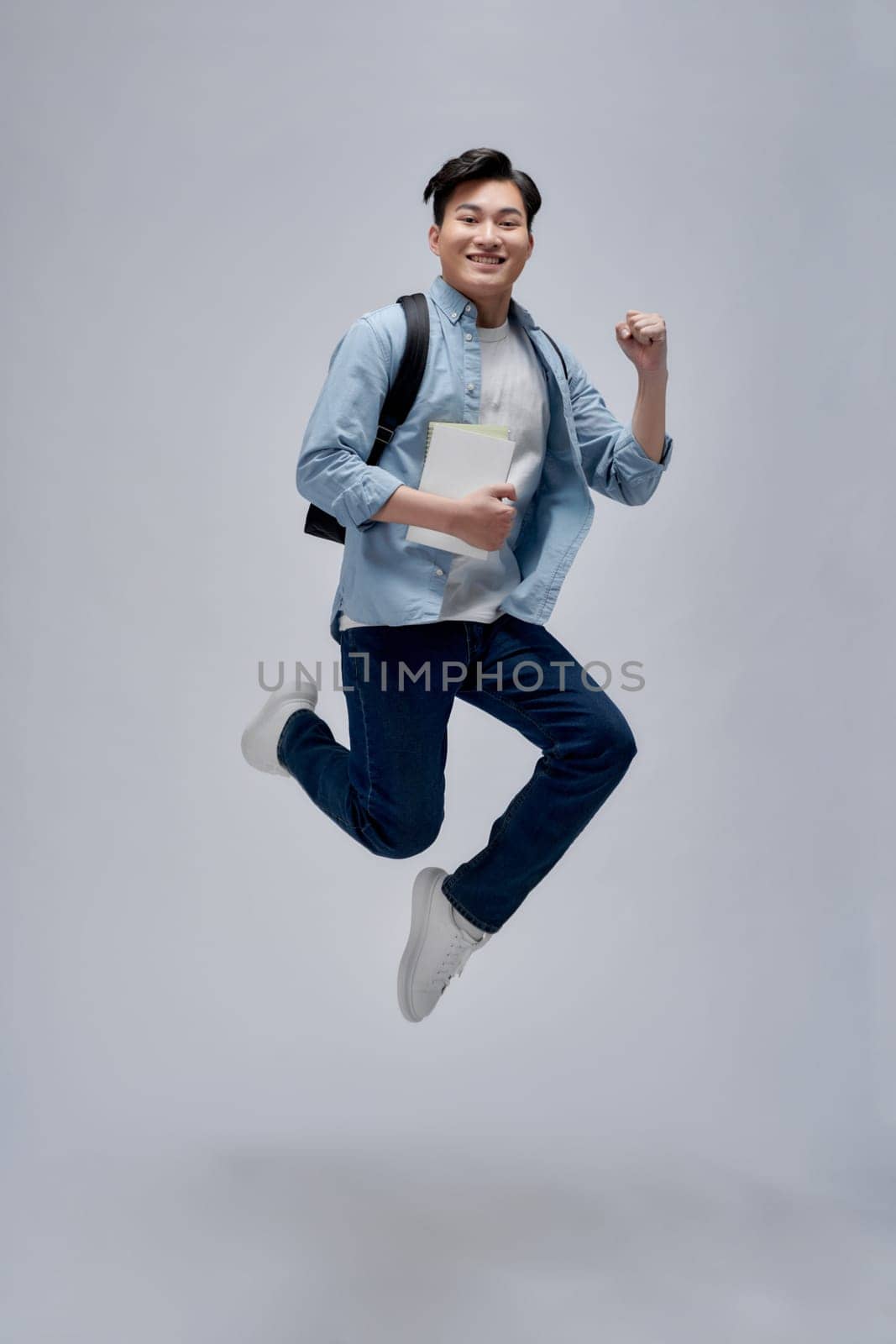 Full length shot of a tall guy holding books and jumping isolated on white background
