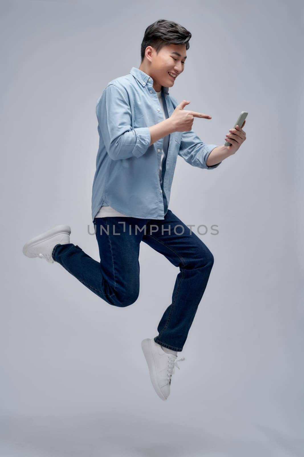 Excited man holding and pointing finger at his cell phone while jumping 