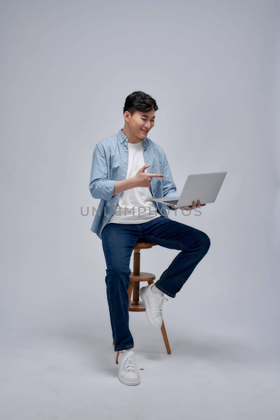 Adult Asian man sitting in a chair smiling confident while pointing to his laptop