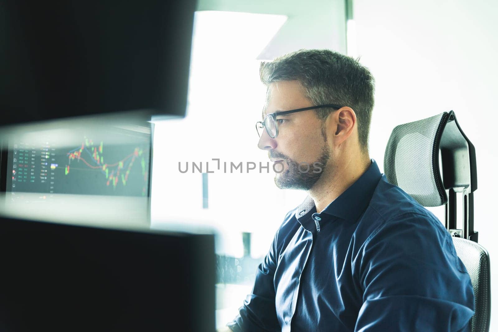 Male stock broker trading online watching charts and data analyses on multiple computer screens.