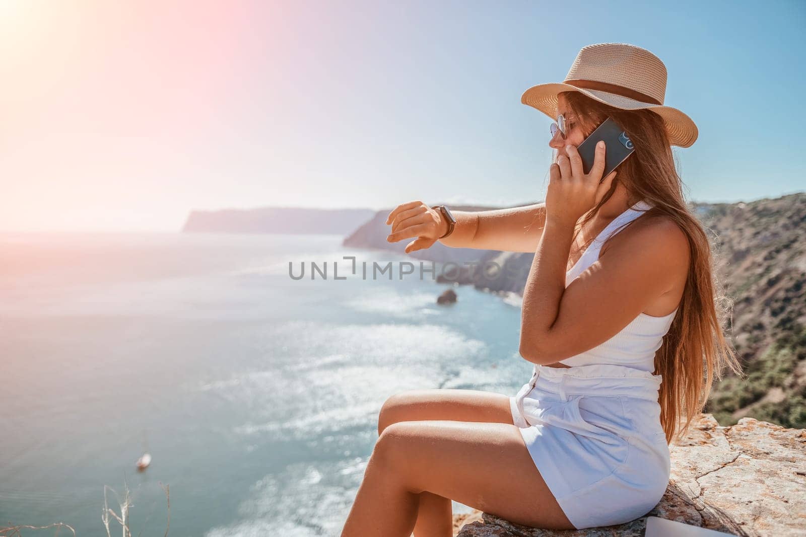 Successful business woman in yellow hat working on laptop by the sea. Pretty lady typing on computer at summer day outdoors. Freelance, travel and holidays concept.