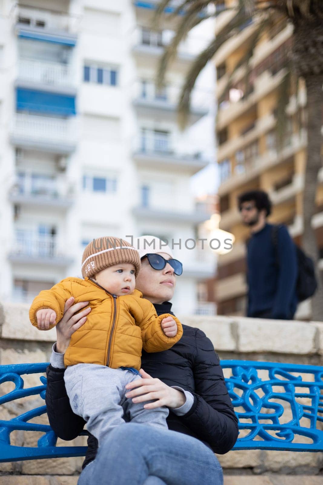 Young mother with her cute infant baby boy child on bench in city park