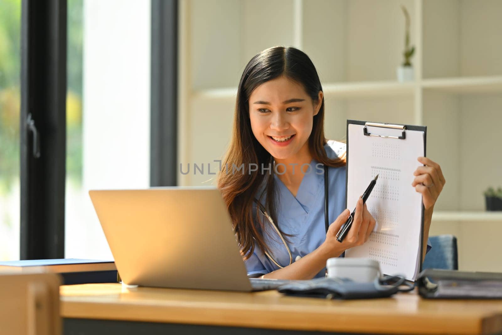 Smiling female doctor having online consultation with patient on laptop in clinic. Tele medical, healthcare and technology.