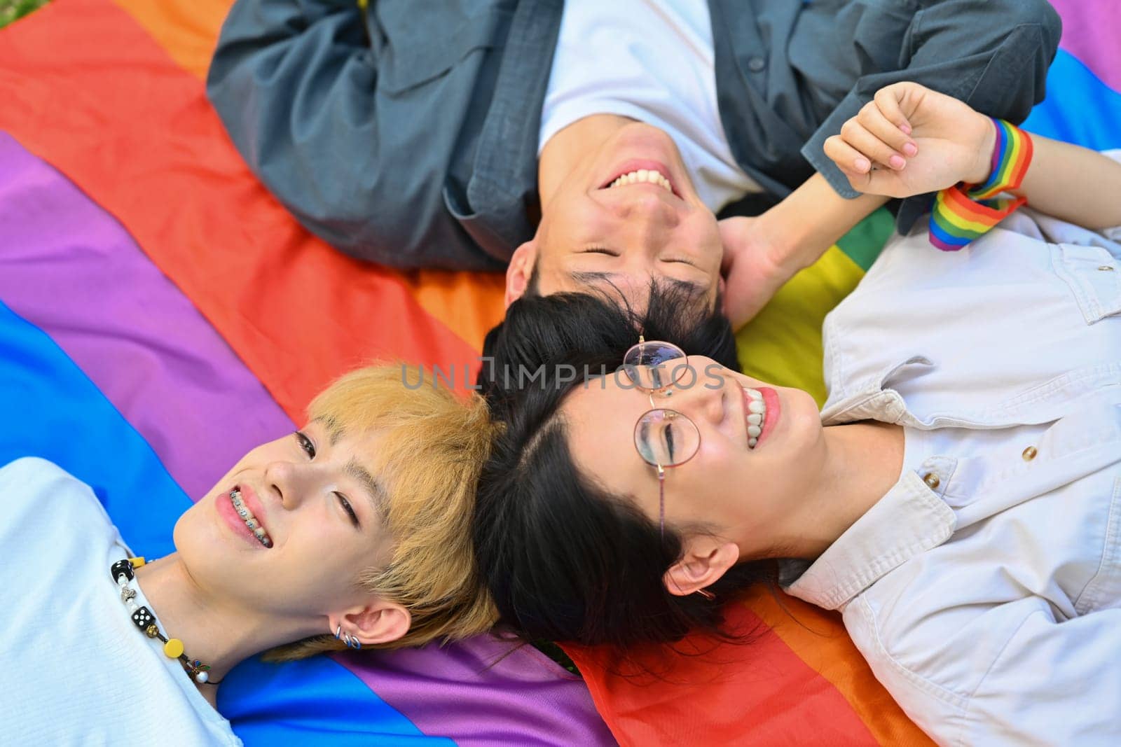 Above view shot of happy young LGBT friends lying on rainbow flag, supporting LGBTQ community and equality social.