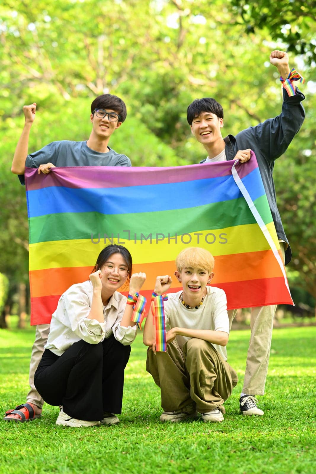 LGBTQ community, freedom, solidarity and equal rights. Image of young people with LGBTQ pride flag, standing in public park.