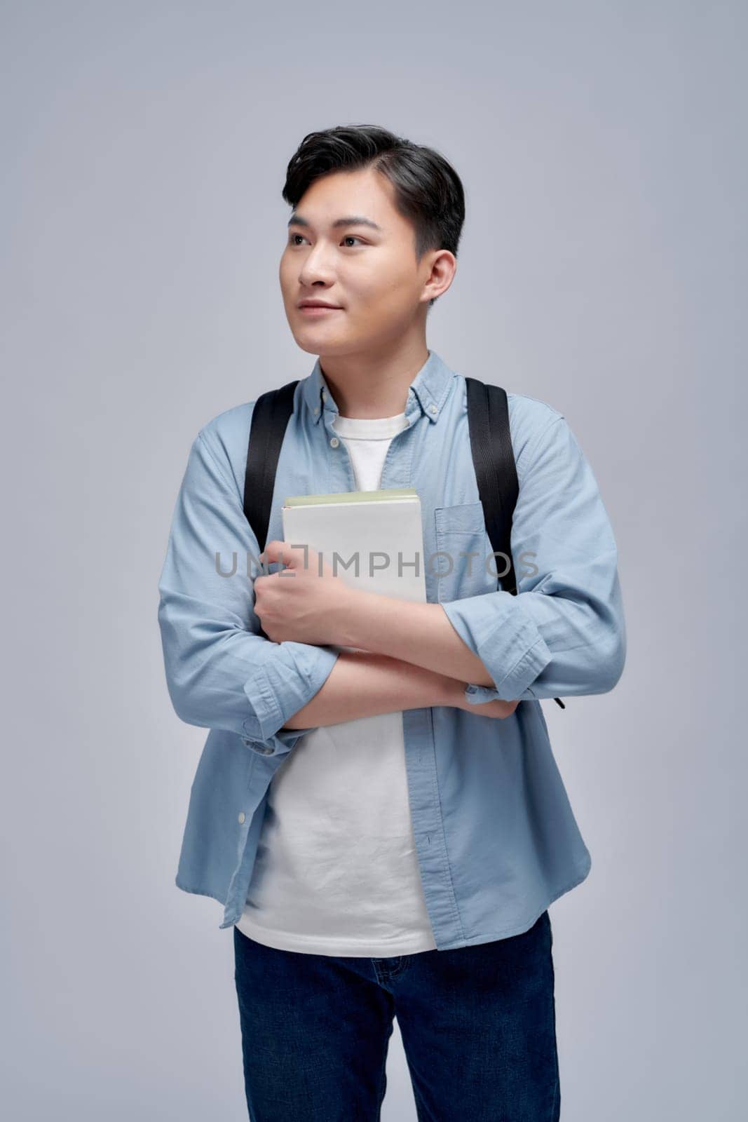 Portrait of smiling young college student with books and backpack against white background
