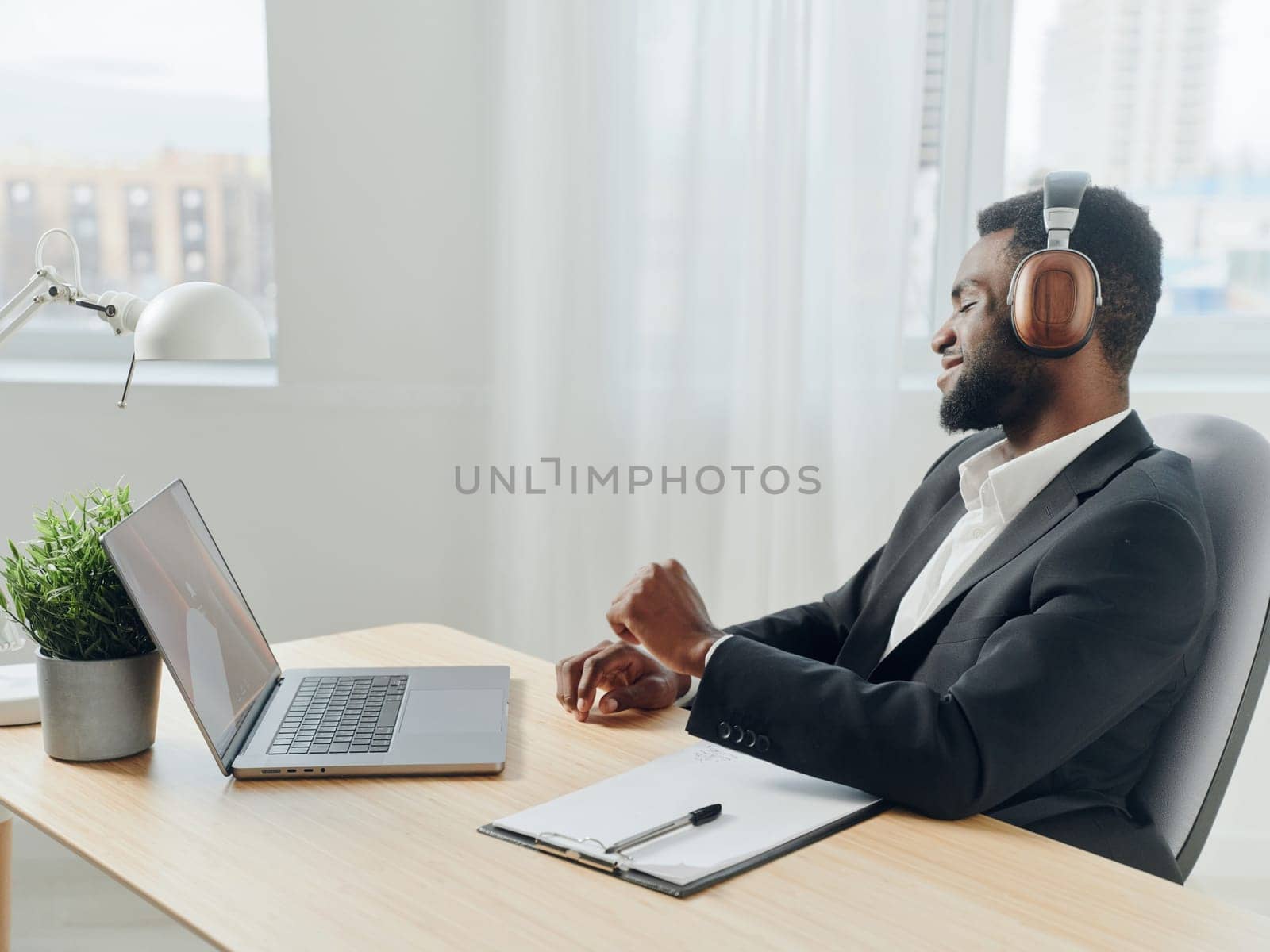 An African-American man sits at his desk in front of his laptop, wearing headphones and chatting on a video call, listening to music. The concept of student business training and online work. High quality photo