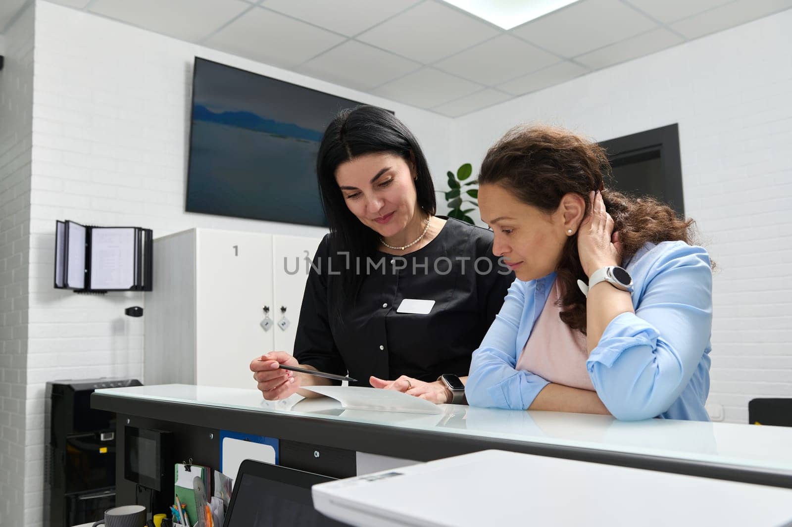 Caucasian confident female dentist hygienist consulting patient, a pregnant woman about the dental treatment that needs to perform during pregnancy in dentistry clinic, standing at reception counter
