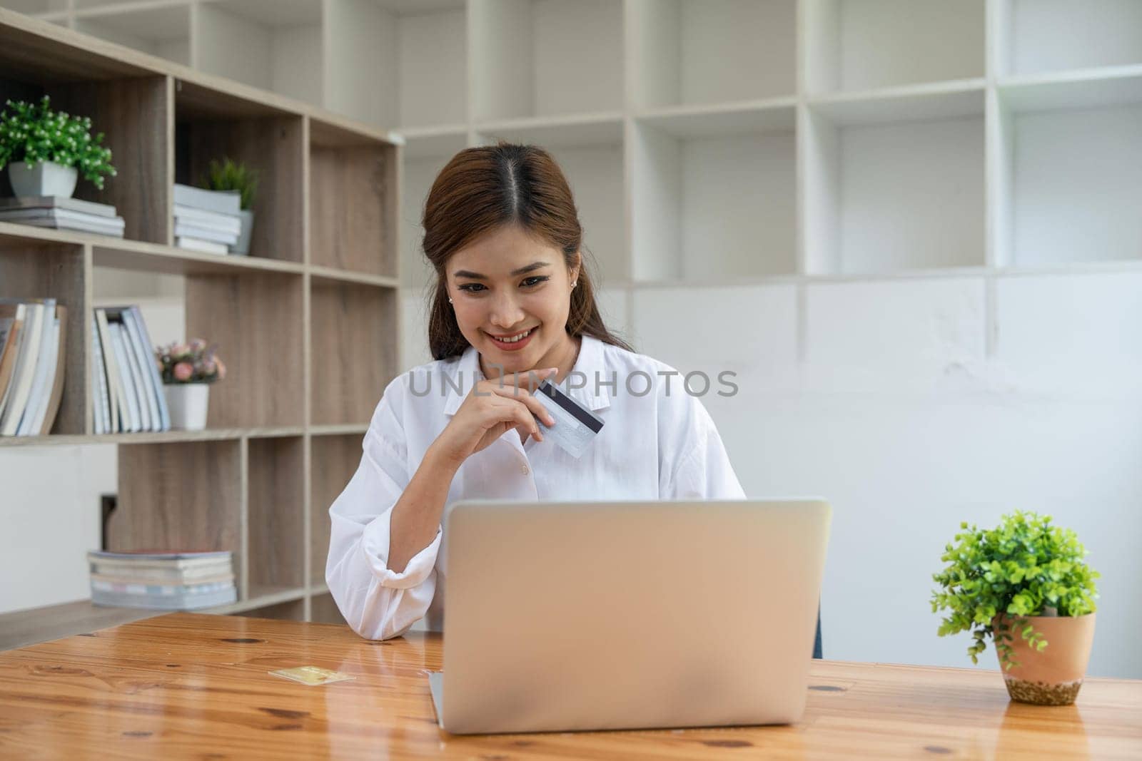 Young adult Asian female consumer holding credit card and laptop at home doing online banking transaction. E commerce virtual shopping, secure mobile banking concept.