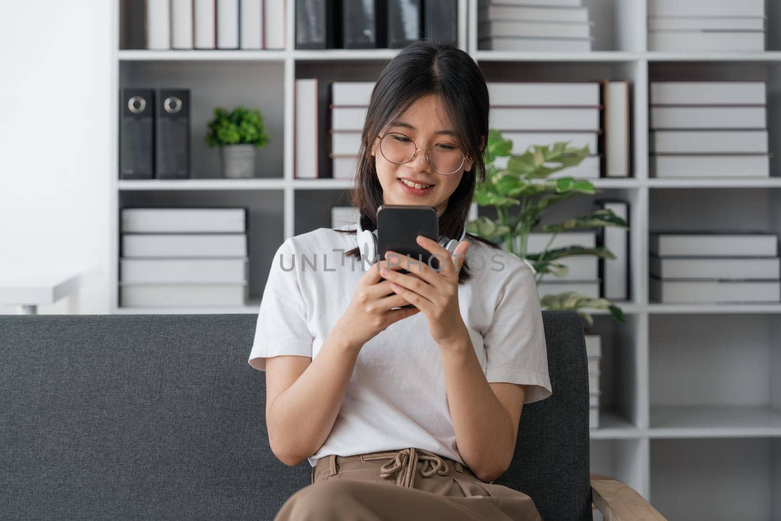 Happy Asian beautiful woman is using mobile phone sitting on a sofa at home.