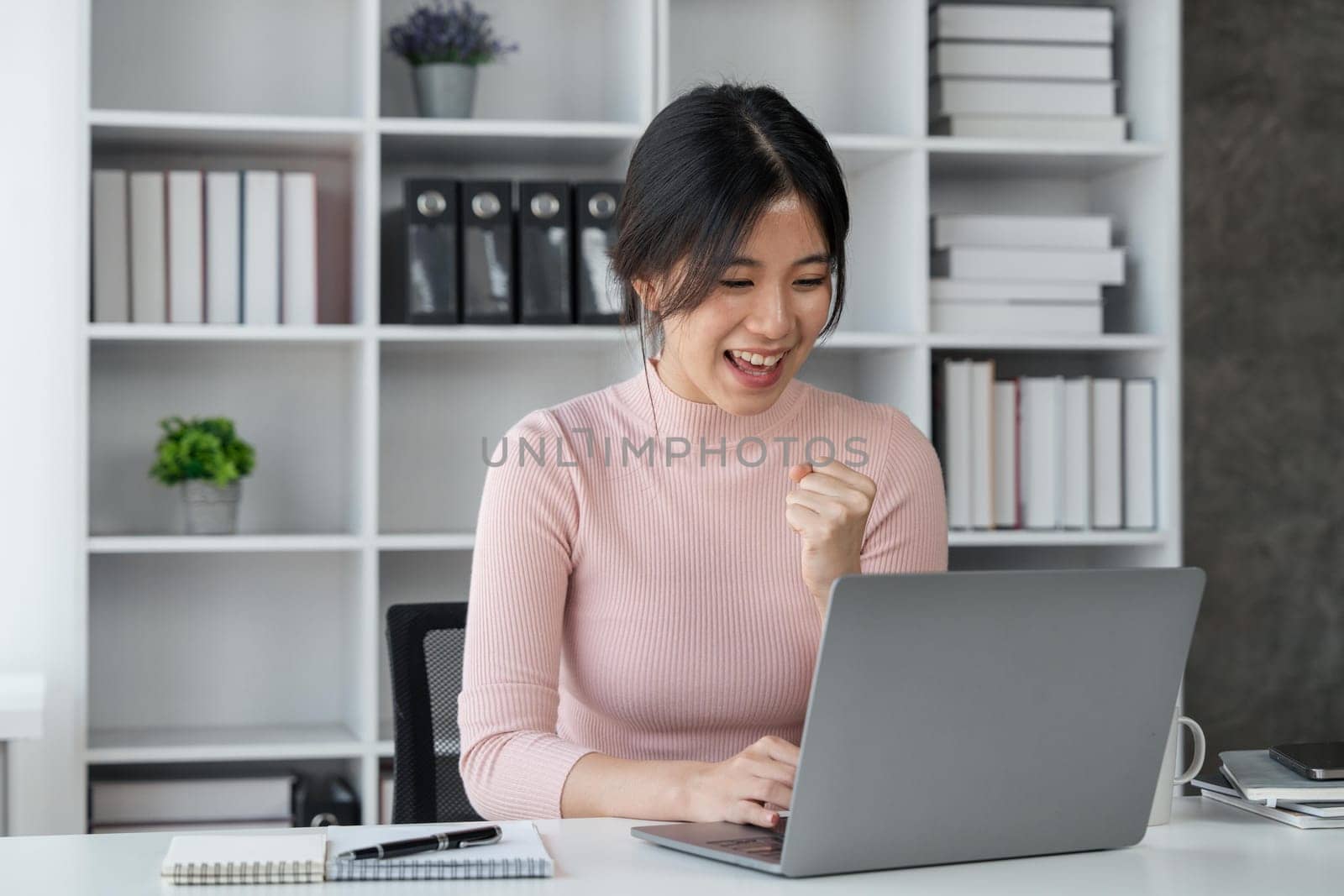 Young asian woman celebrating winning or getting ecommerce shopping offer on computer laptop. Excited happy girl winner looking at notebook celebrating success..