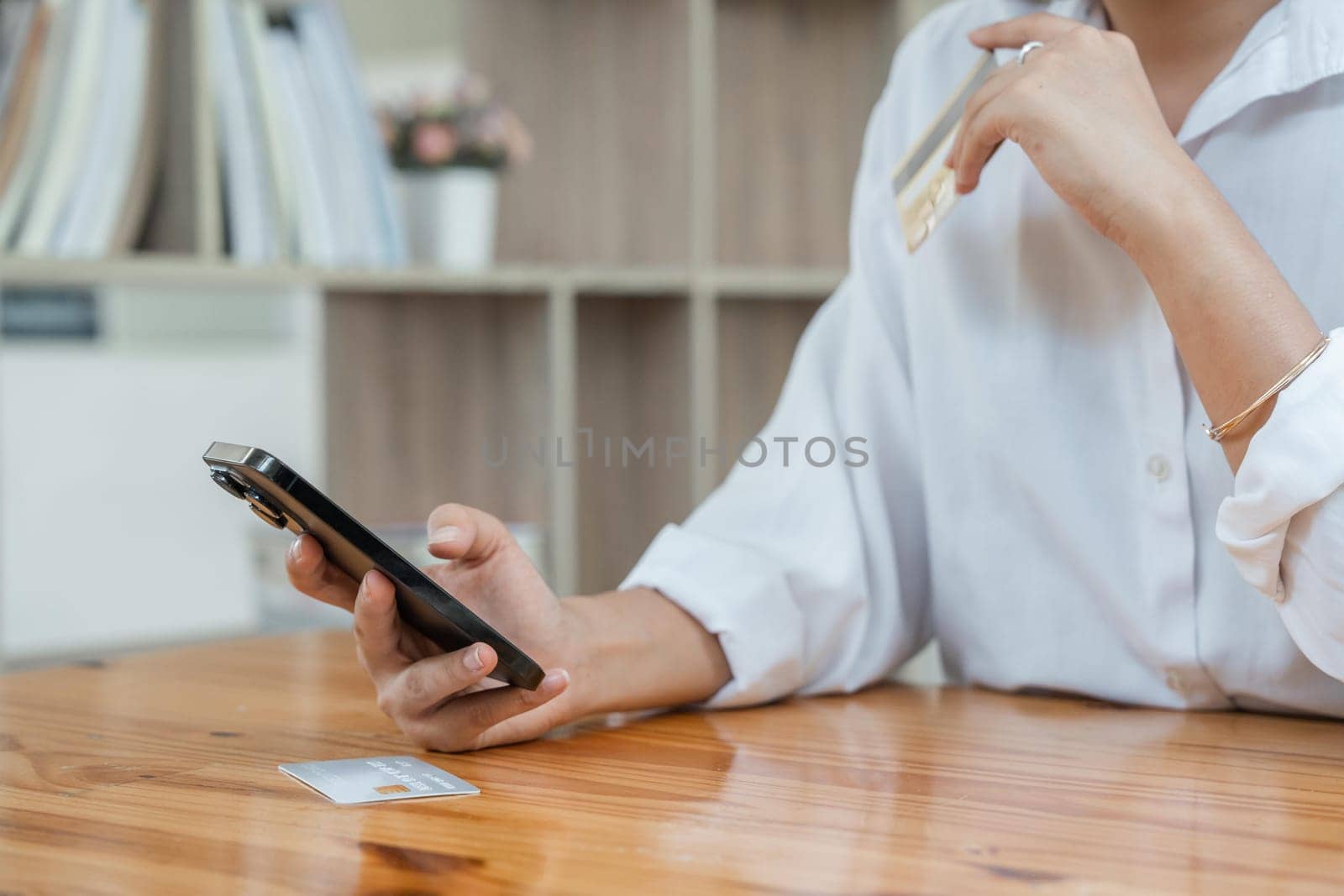 Young adult Asian female consumer holding credit card and smartphone at home doing online banking transaction. E commerce virtual shopping, secure mobile banking concept.