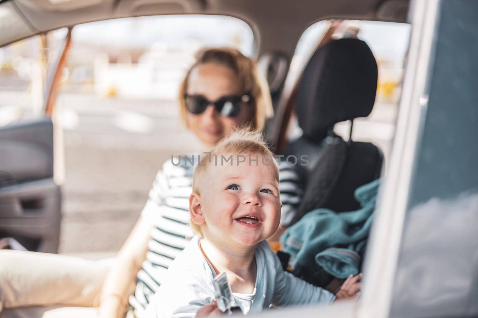 Mother and her infant baby boy child on family summer travel road trip, sitting at dad's front seat, waiting in the car for father to buy farry tickets