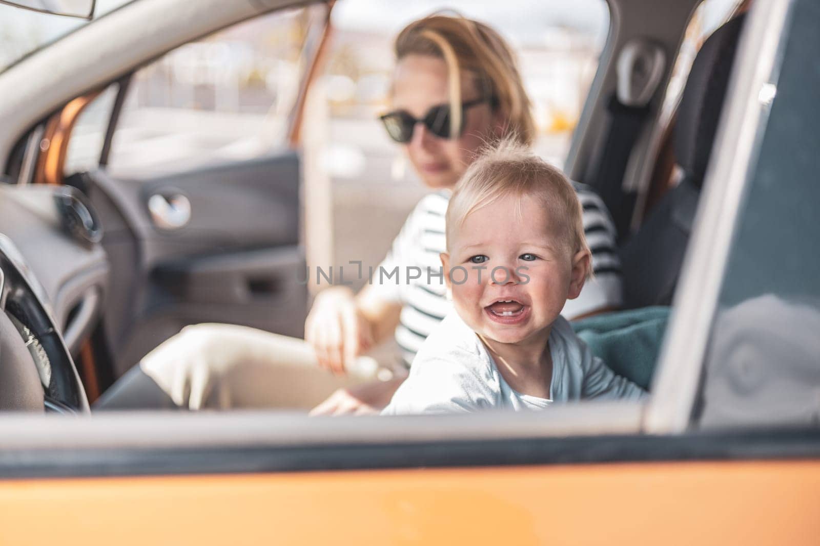 Mother and her infant baby boy child on family summer travel road trip, sitting at dad's front seat, waiting in the car for father to buy farry tickets