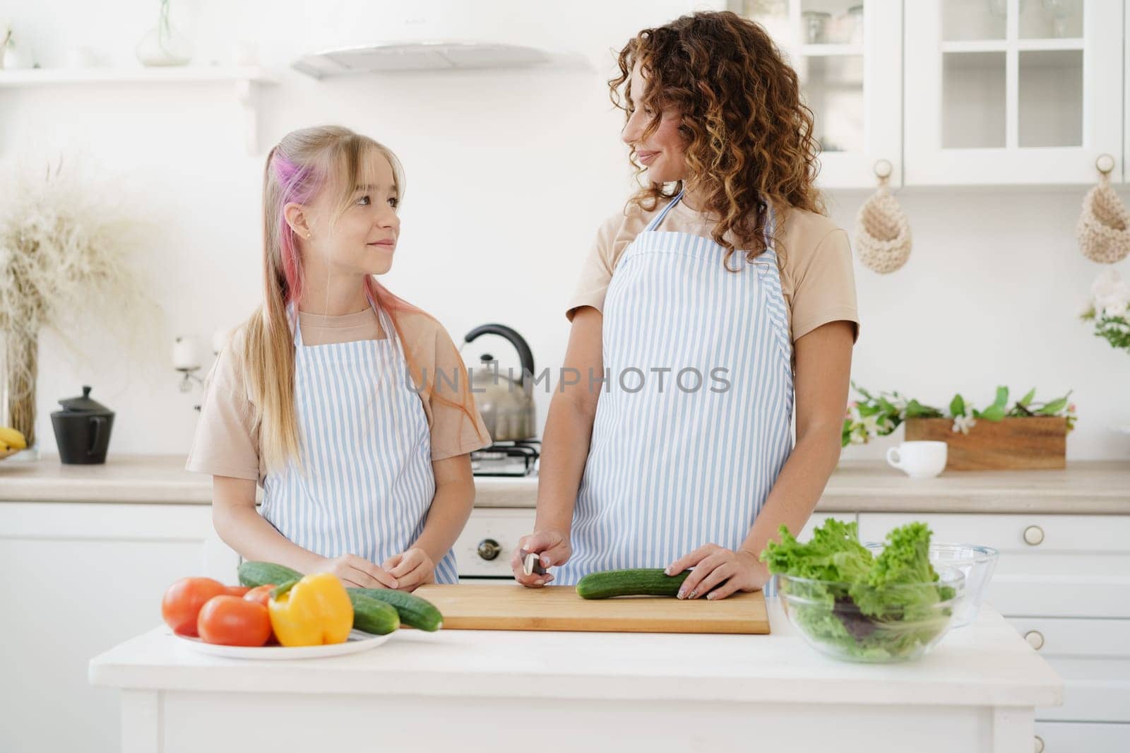 Mother and teen daughter preparing vegetable salad at kitchen, close up
