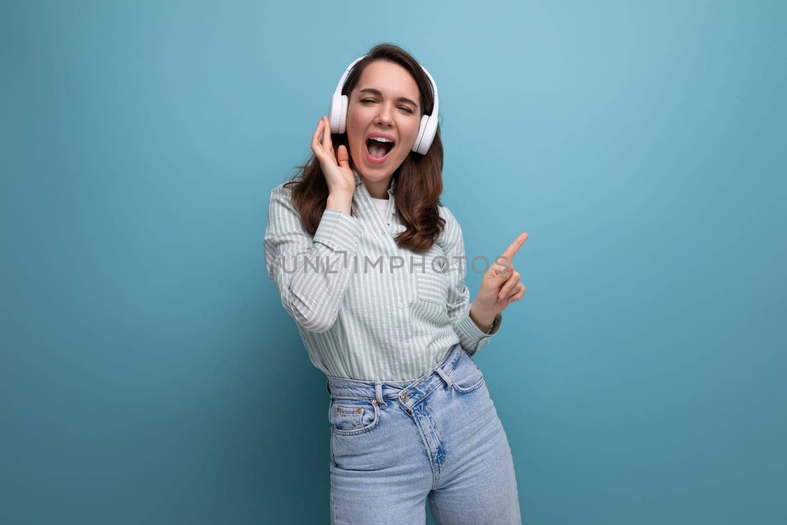 20s brunette lady in shirt and jeans listening to playlist in wireless headphones.