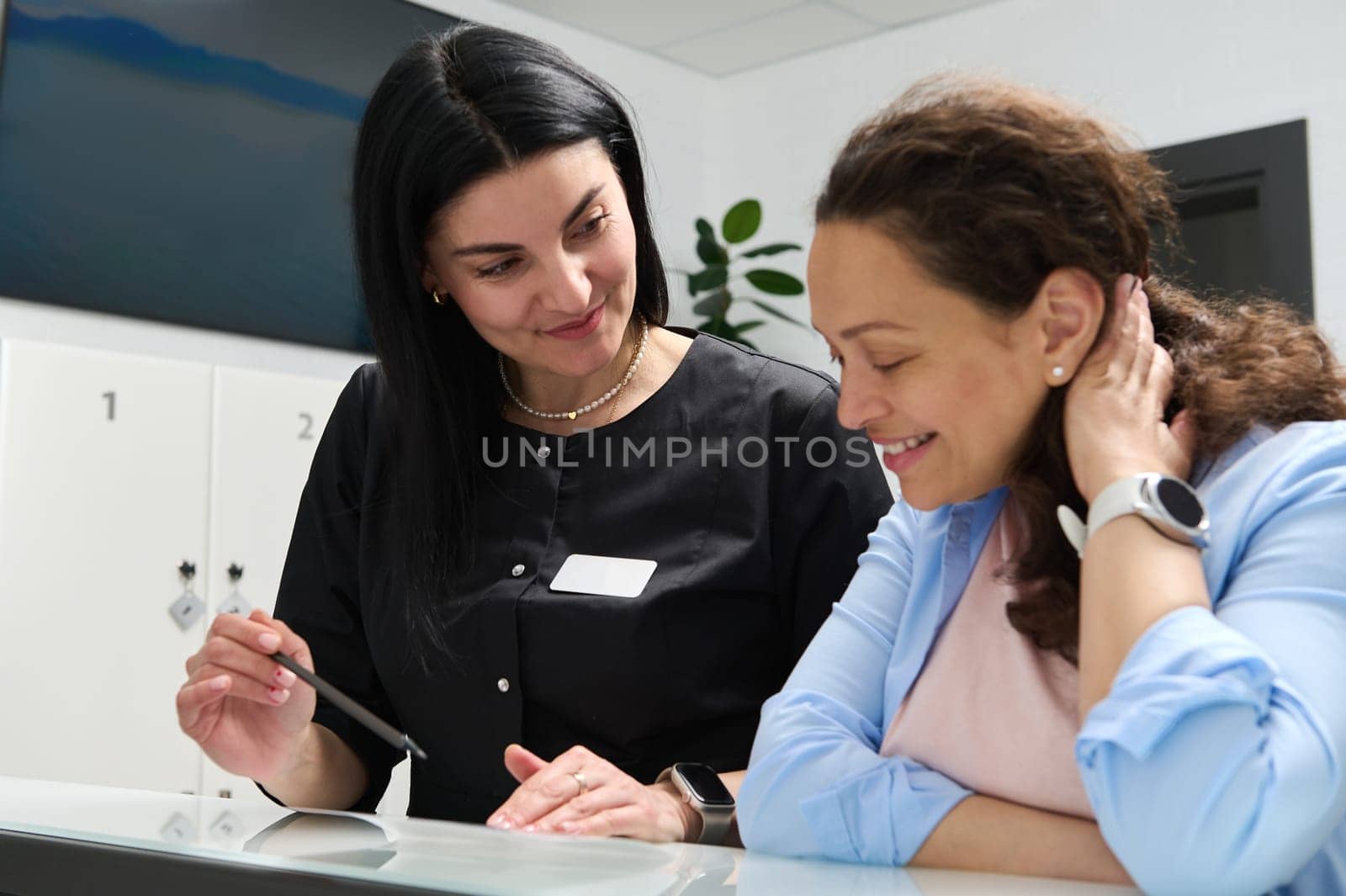 Smiling pleasant woman doctor dentist talking to a female patient, explaining the prescribed treatment, filling out forms standing at reception counter in modern dental clinic or outpatient hospital.