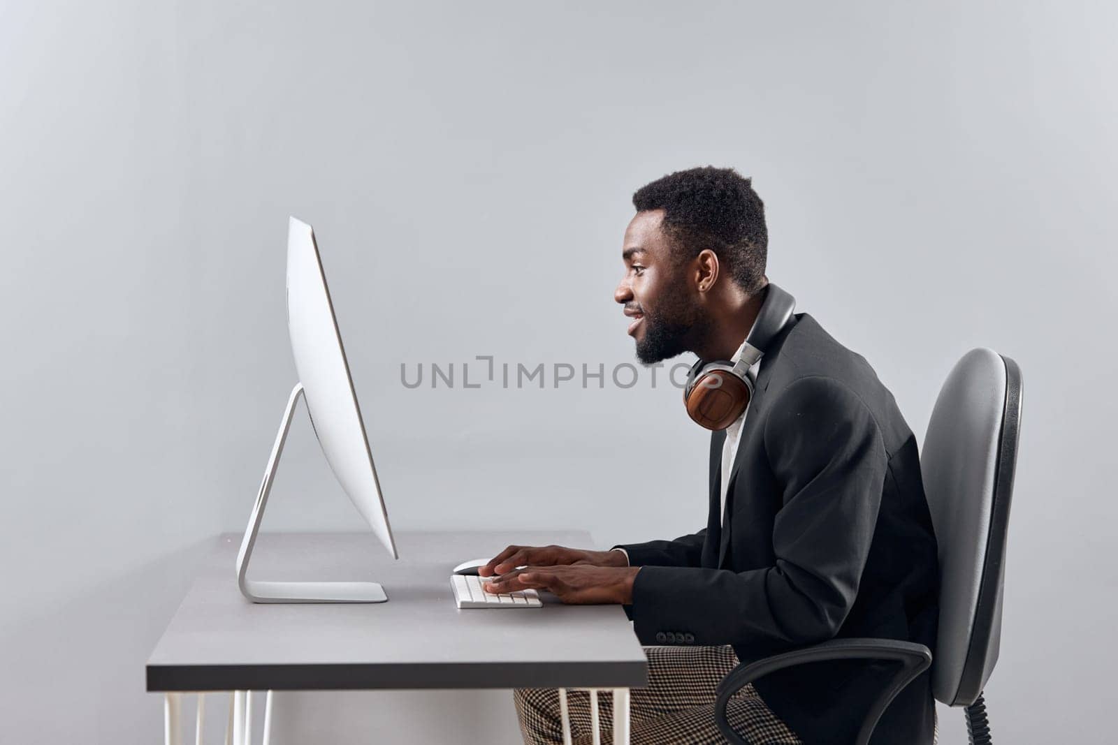 An African-American man sits at his desk in front of his laptop, wearing headphones and chatting on a video call, listening to music. The concept of student business training and online work. High quality photo