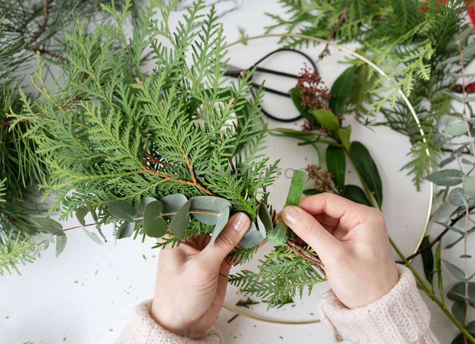 The process of making a Christmas wreath from needles, thuja, shimia, rosehip, pine twigs, chopped twigs for the wreath. The concept of preparation for Christmas and New Year