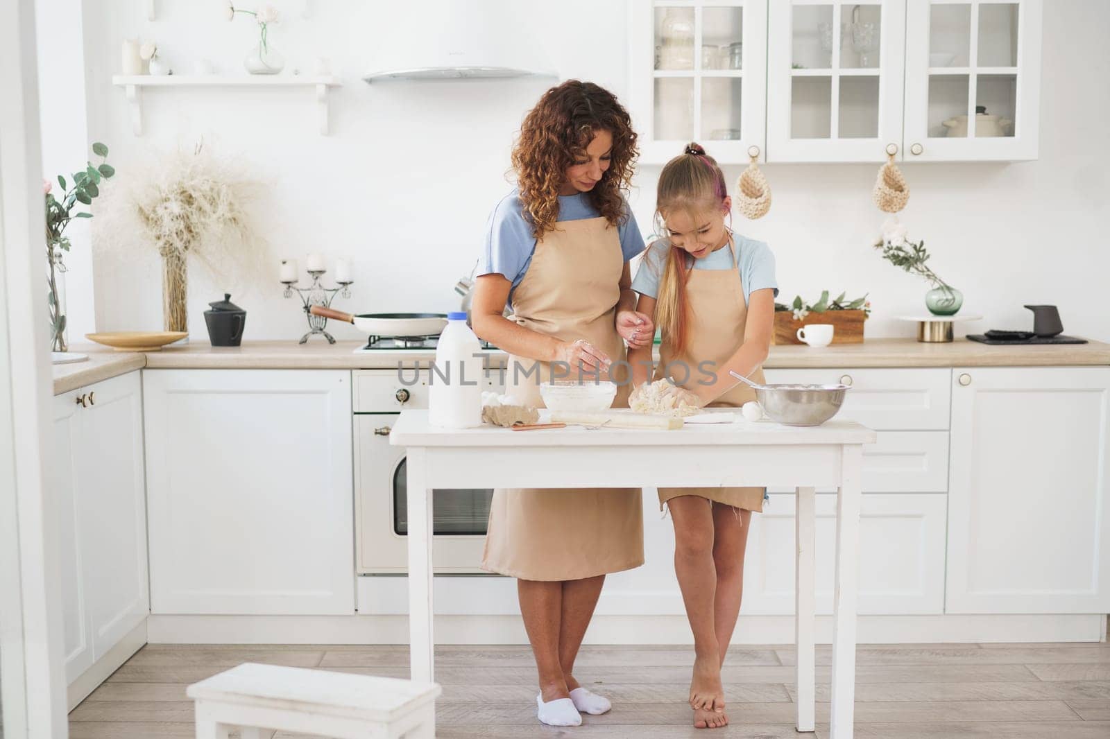 Teen girl helping her mom to cook dough in their kitchen at home, close up