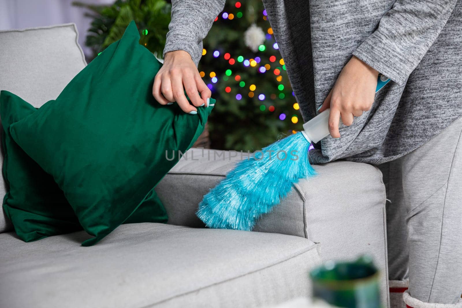 During a thorough cleaning, a woman picks up a pillow and sweeps up dust lying on the sofa. Taking care of order and tidiness throughout the house during all kinds of world.