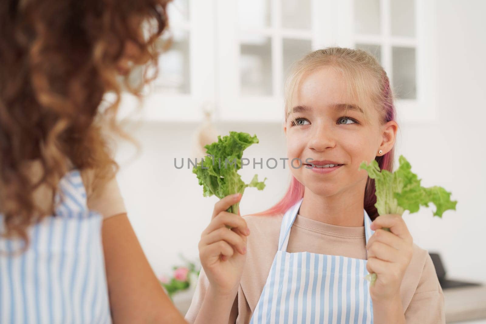 Mother and daughter playing and having fun with vegetables in kitchen by Fabrikasimf