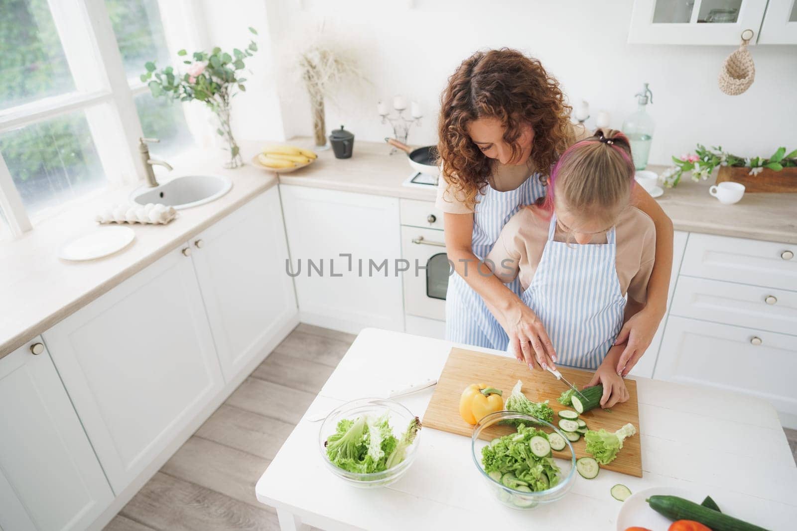 Mommy teaching her teen daughter to cook vegetable salad in kitchen by Fabrikasimf