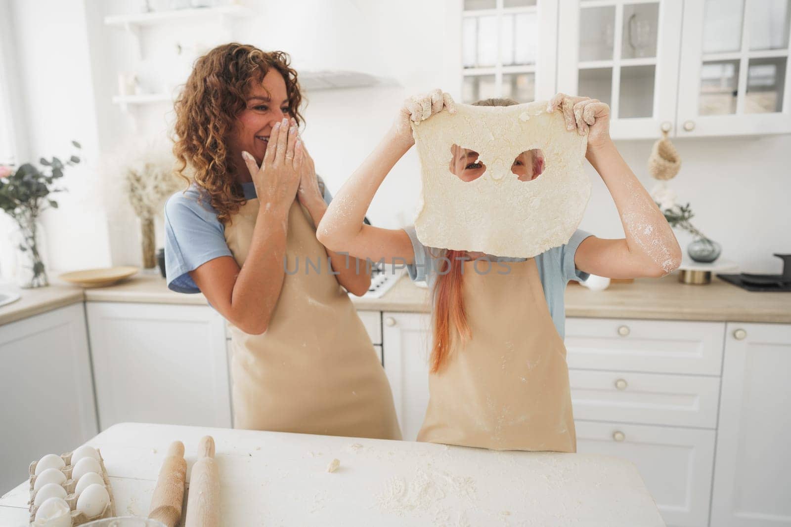 Mother and daughter having fun while cooking dough in kitchen by Fabrikasimf