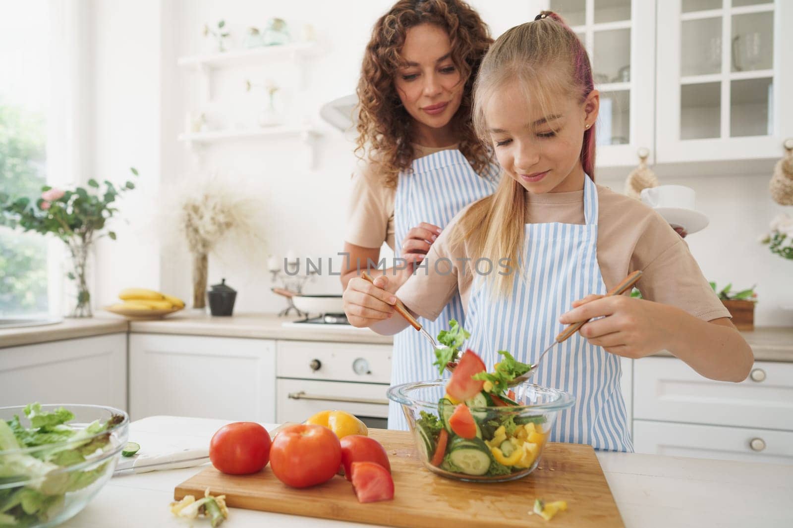 Mommy teaching her teen daughter to cook vegetable salad in kitchen, close up