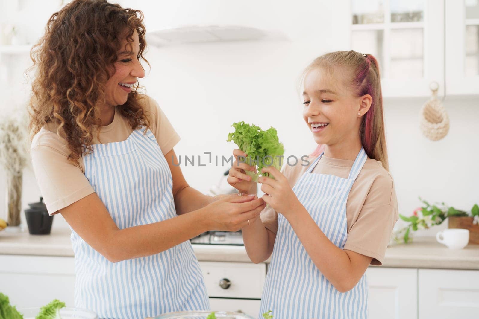 Mother and daughter playing and having fun with vegetables in kitchen while cooking