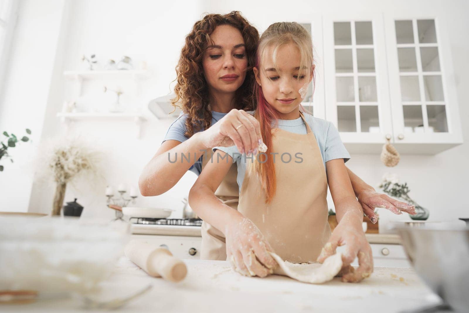Teen girl helping her mom to cook dough in their kitchen at home, close up