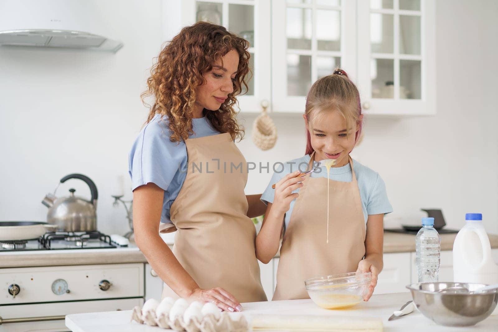 Mother and teen daughter making dough for pastry toghether in kitchen by Fabrikasimf