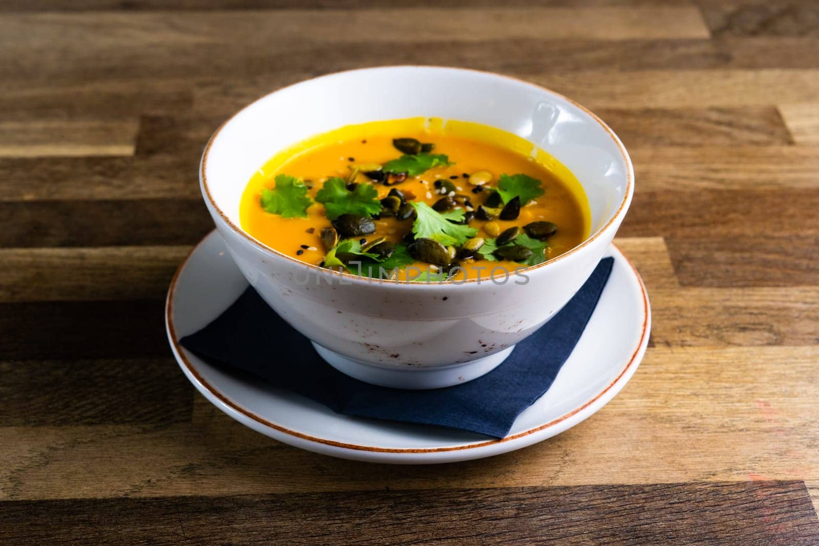 Pumpkin and carrot soup with cream and parsley on dark wooden background by Zelenin