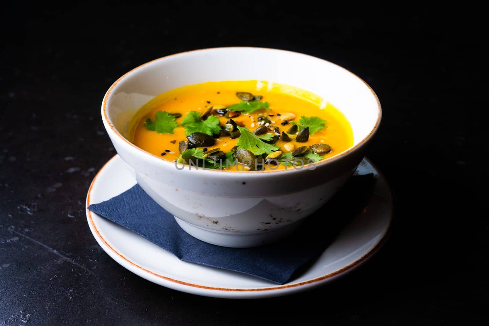 Pumpkin and carrot soup with cream and parsley on a dark wooden background