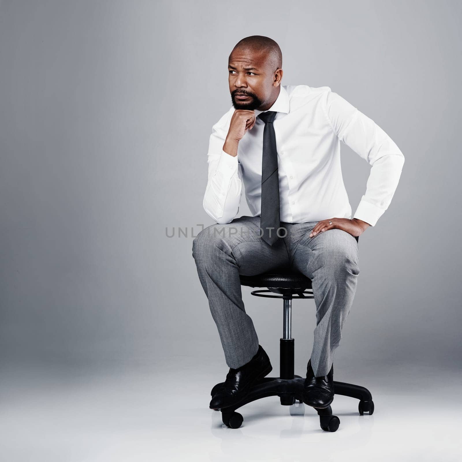 The price of success is hard work and determination. Studio shot of a corporate businessman sitting on a chair against a grey background