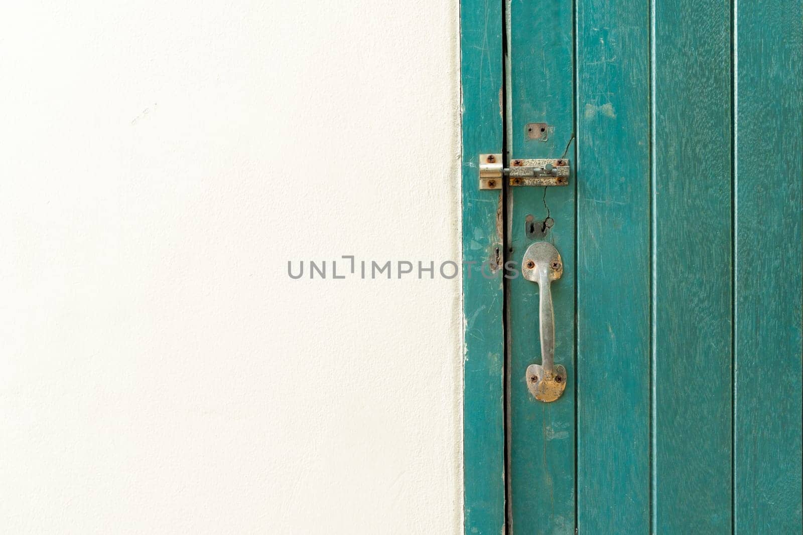 Closed padlock hangs on the green color wooden door and wall.