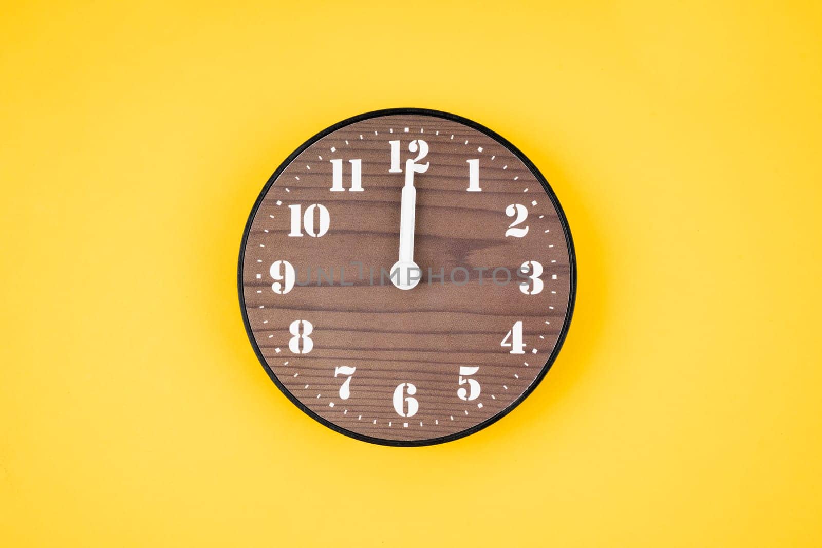 The Retro wooden clock at 12 O' clock on yellow color background. by Gamjai