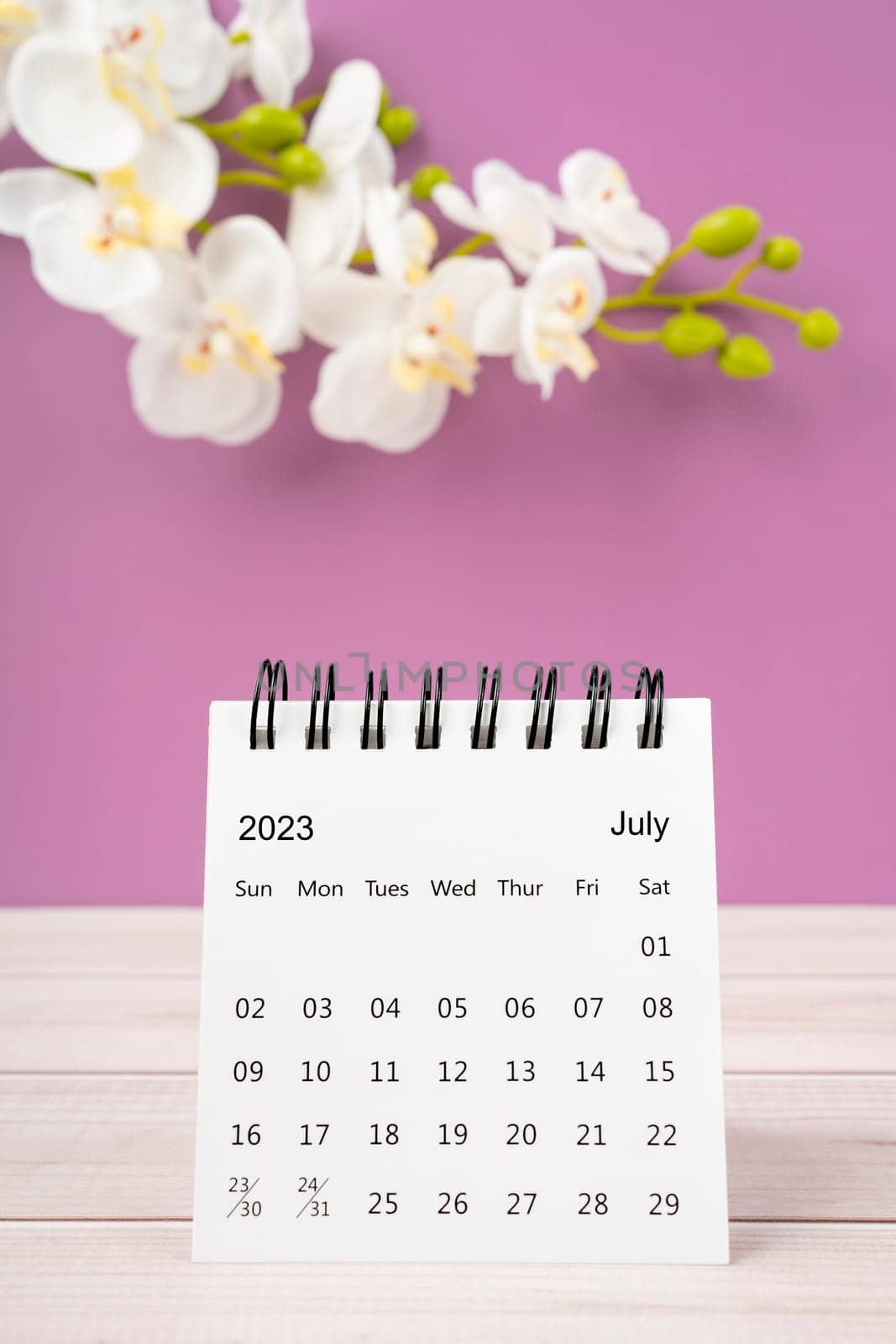 July 2023 desk calendar and white orchid flower on wooden background.