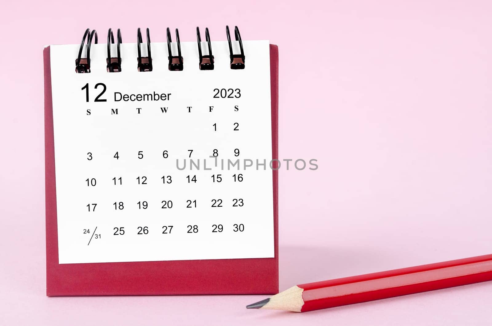 December 2023 desk calendar and wooden pencil on pink color background.