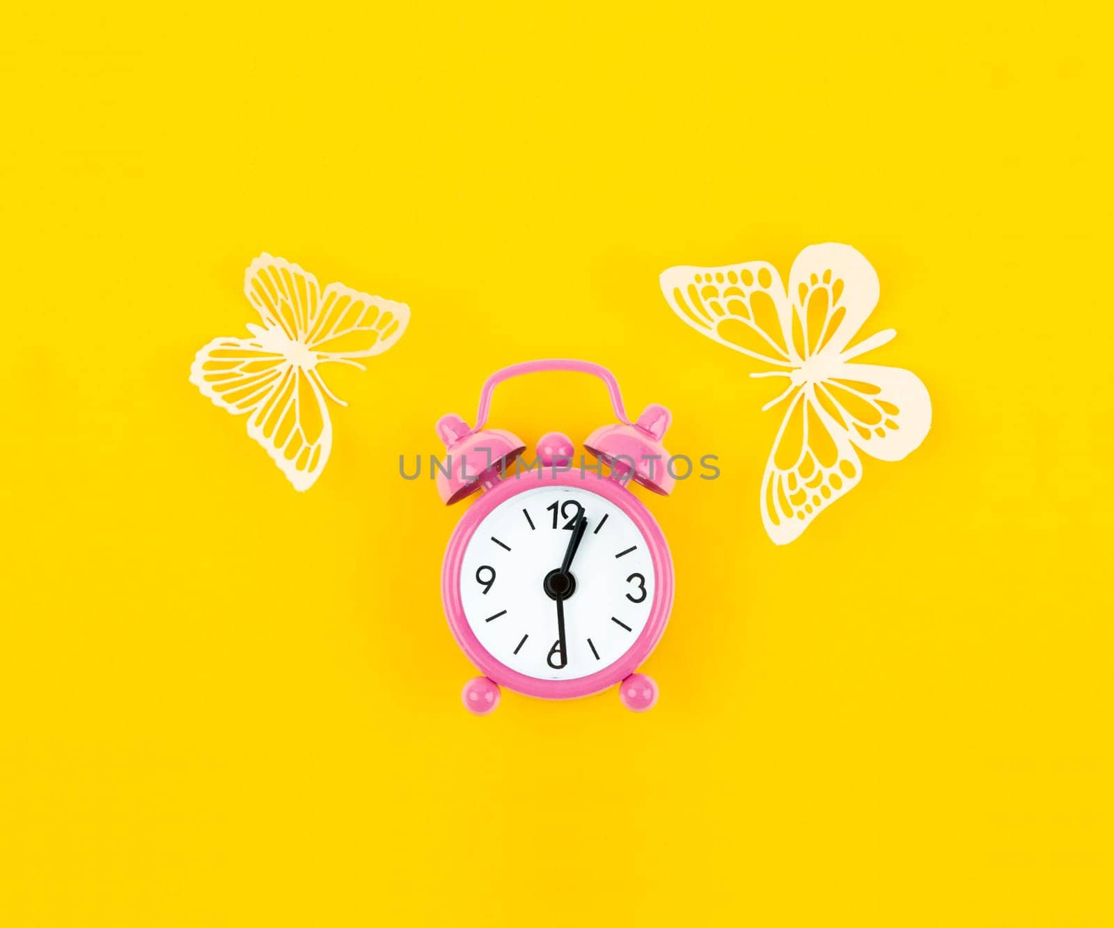 Pink alarm clock and paper butterflies on a yellow background.